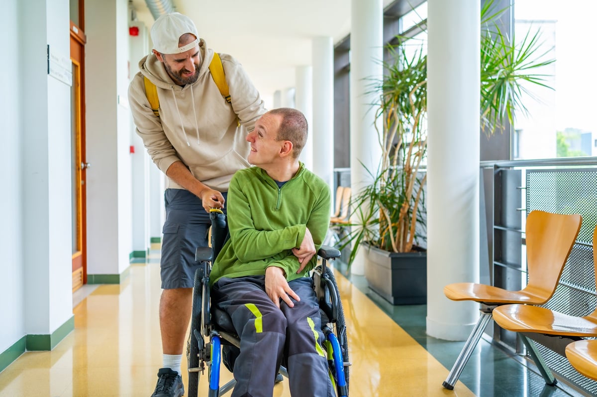 Young man pushing a friend in a wheelchair at a university campus