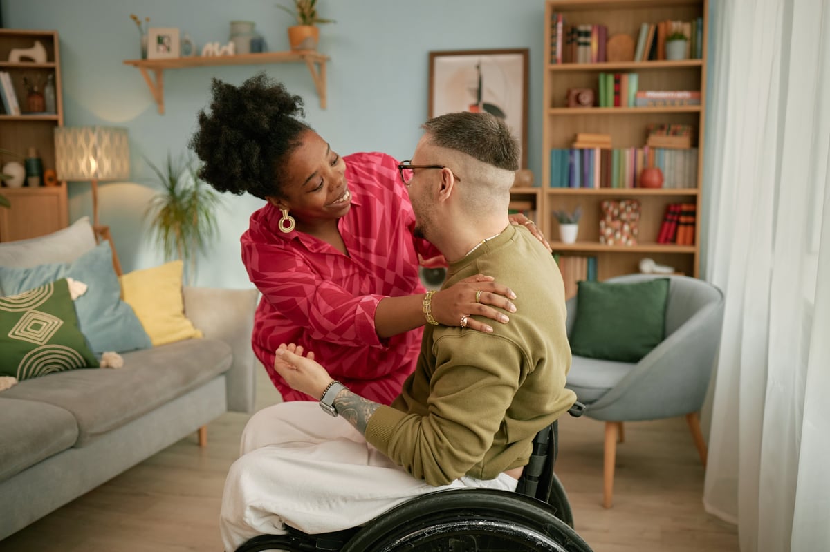 A woman smiling and embracing a man in a wheelchair during a celebration